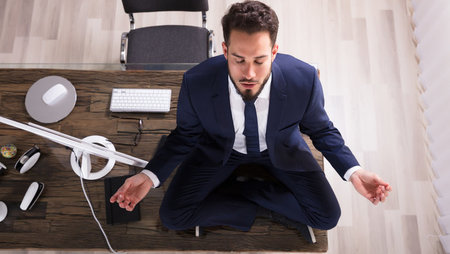Young businessman sitting on his desk and doing yoga in the office